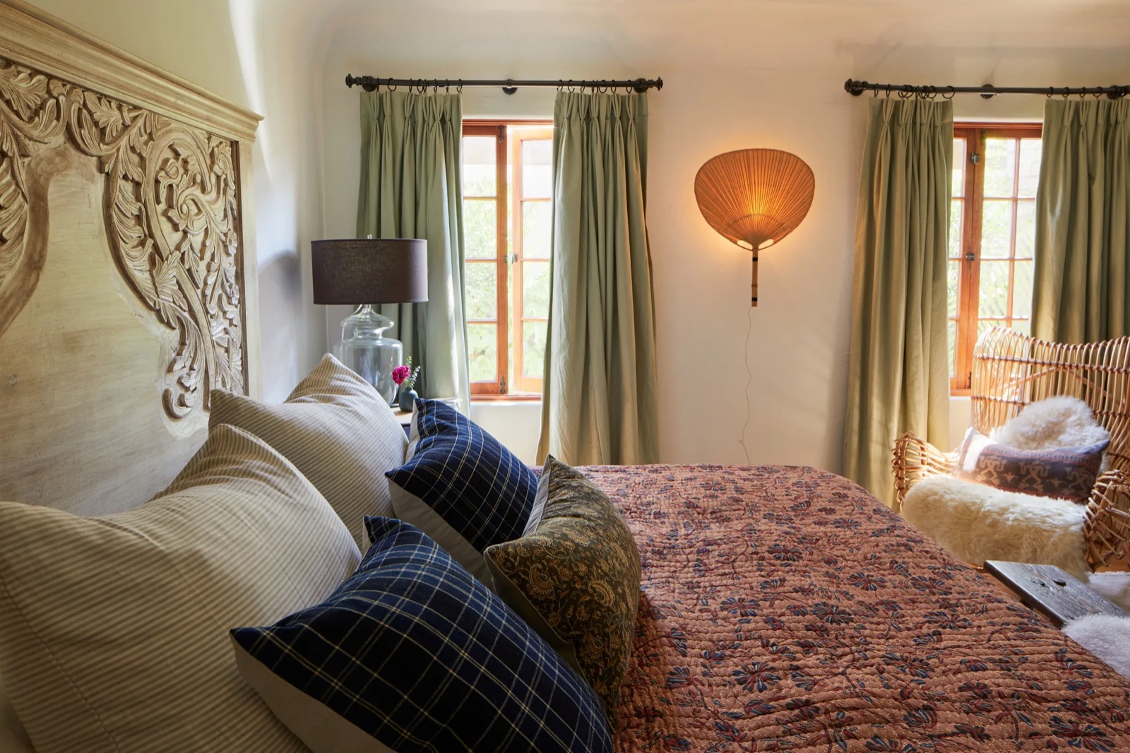 A bedroom with a carved headboard and sage curtains, a project by Charlie Barstein